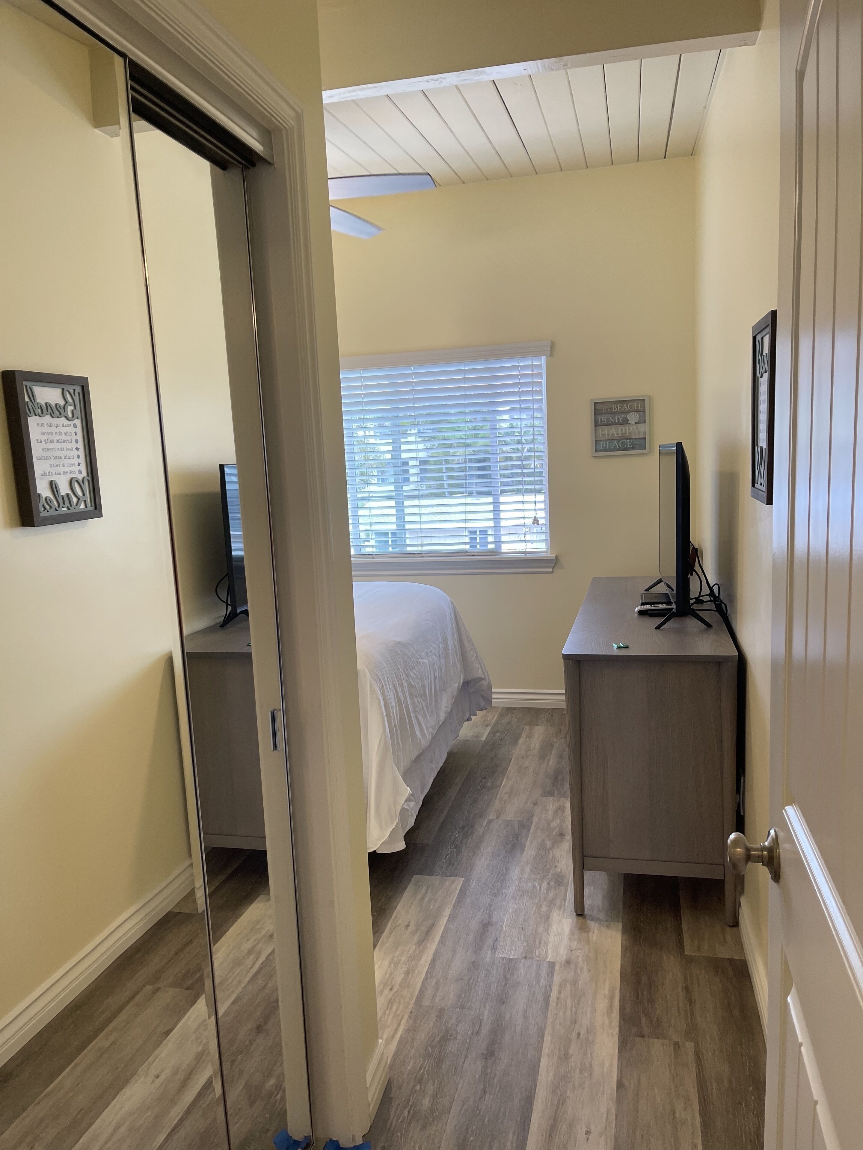 A bedroom with a bed, a desk, a computer, and a window with blinds.