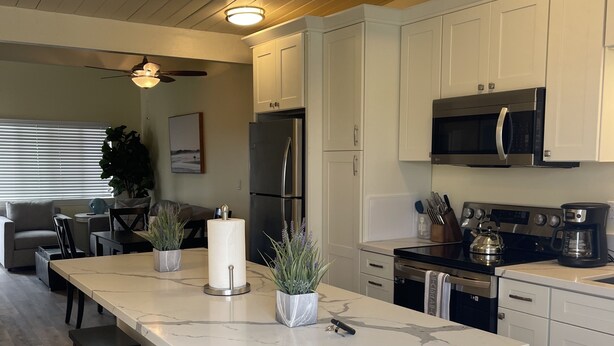 A modern kitchen with white cabinets, a large island with bar stools, a refrigerator, a microwave, and a coffee maker. - Ultimate Beach Vacation in the Heart of Carlsbad  (Carlsbad)