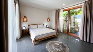 Un dormitorio con cama de madera, dos mesitas de noche con lámparas, un tapete redondo tejido y un ventanal corredero que da a un balcón con plantas.