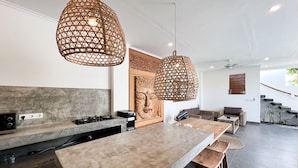 Una cocina moderna con una isla grande, luces colgantes y una escalera que sube a un nivel superior.