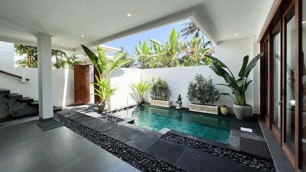 Un área de piscina interior moderna con una vista despejada del cielo, rodeada de plantas en macetas y un camino de piedra.