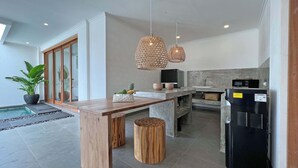 Una cocina moderna con una isla de madera, dos lámparas colgantes de mimbre y un refrigerador negro.
