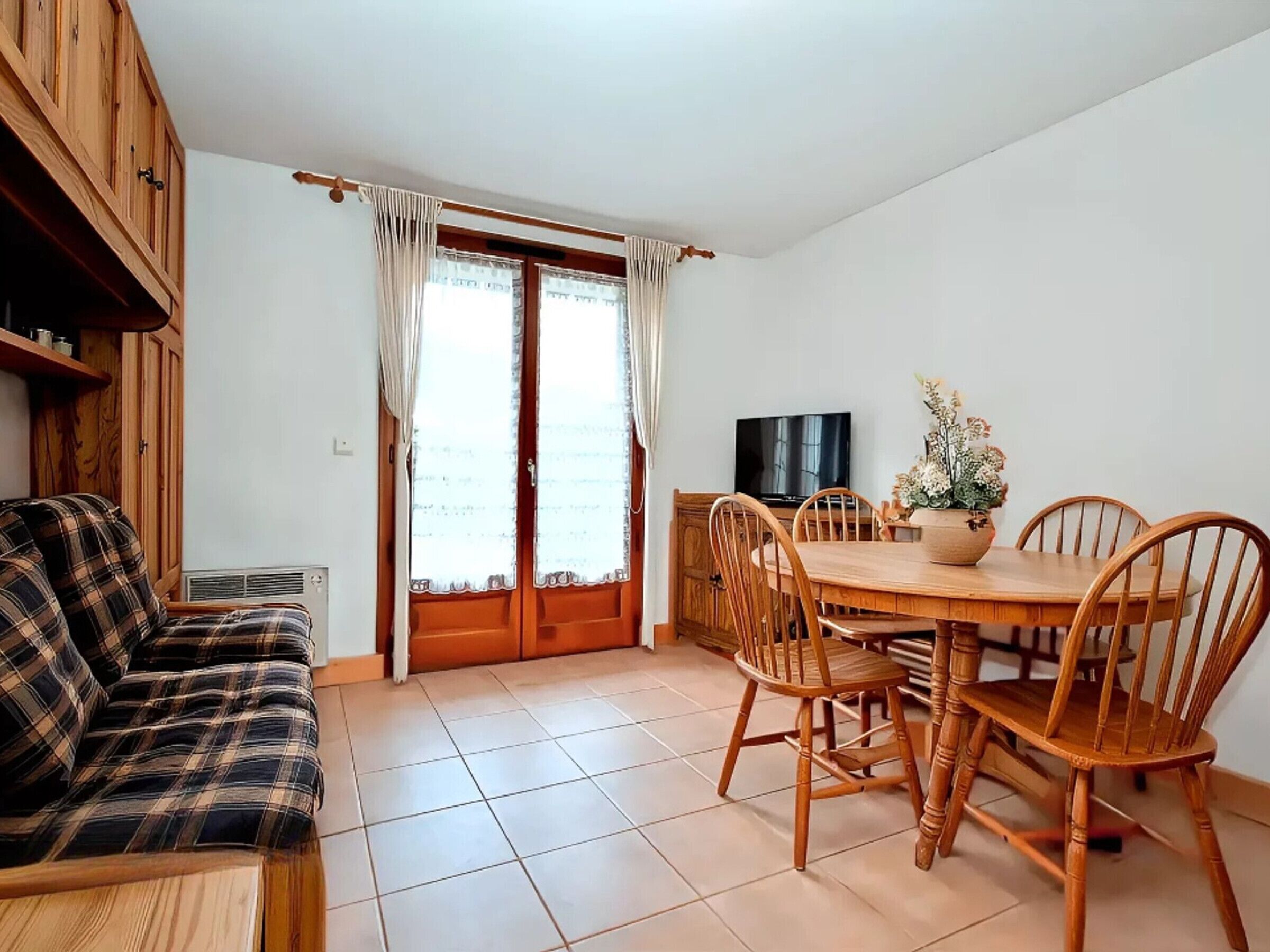 Una sala de estar acogedora con un sofá, una mesa de comedor con sillas, un televisor y una ventana con cortinas.