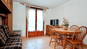 Un salon confortable avec un canapé, une table à manger et des chaises, un téléviseur et une fenêtre avec des rideaux.
