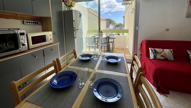 A compact kitchen with modern appliances, a dining table set for four, and a red sofa in the living area.