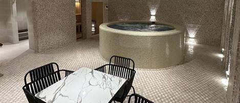 Un área de spa con una mesa y sillas de mármol, una bañera de hidromasaje y una pared con textura.