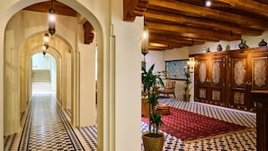 A hallway with a checkered floor and arches, leading to a room with a red carpet and wooden cabinets. - Kosh Havuz Boutiqe Hotel (Samarkand)