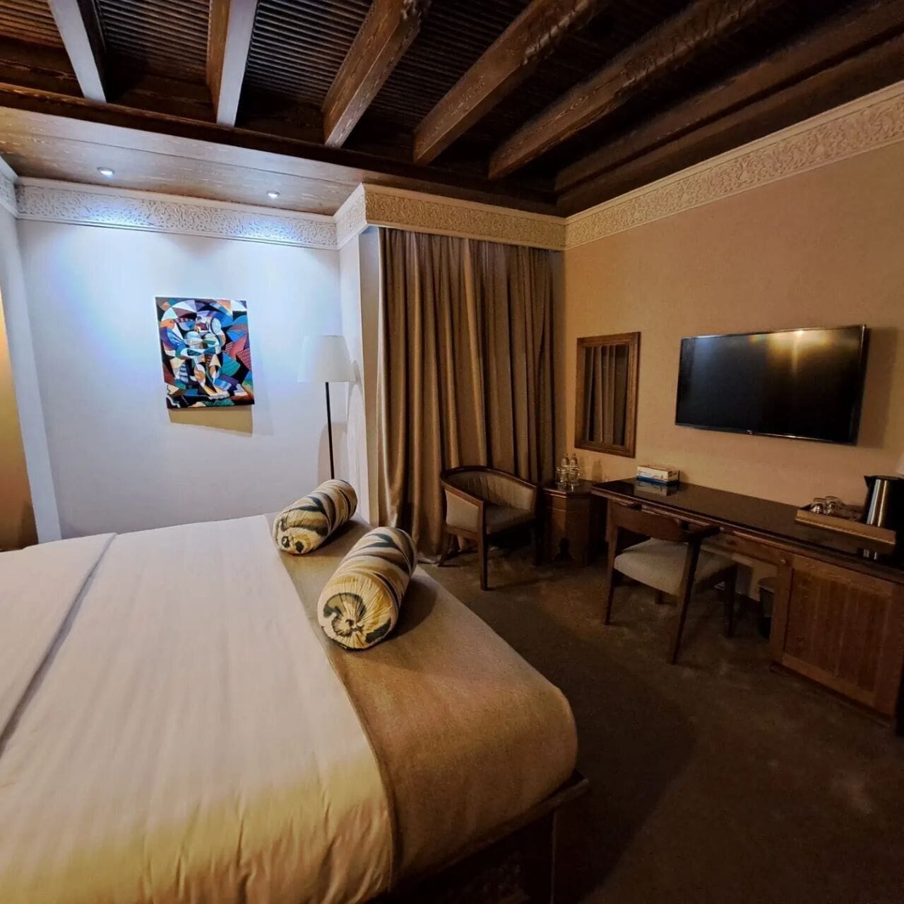 A hotel room with a large bed, a desk, a chair, a television, and a painting on the wall.