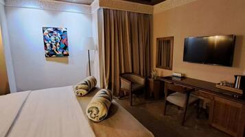 A hotel room with a large bed, a desk, a chair, a television, and a painting on the wall.