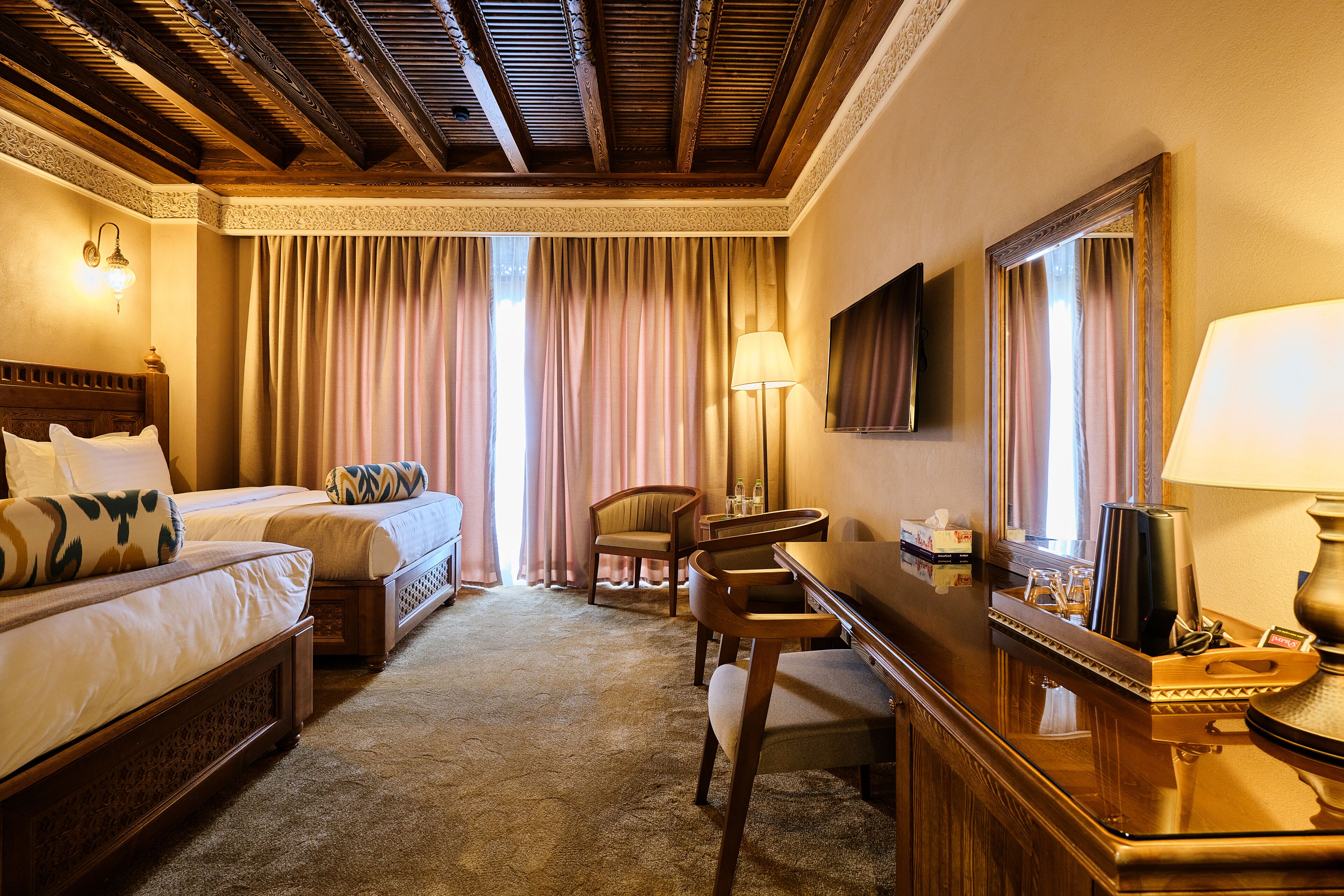 Hotelkamer met twee bedden, een bureau, een stoel, een lamp en een grote spiegel.