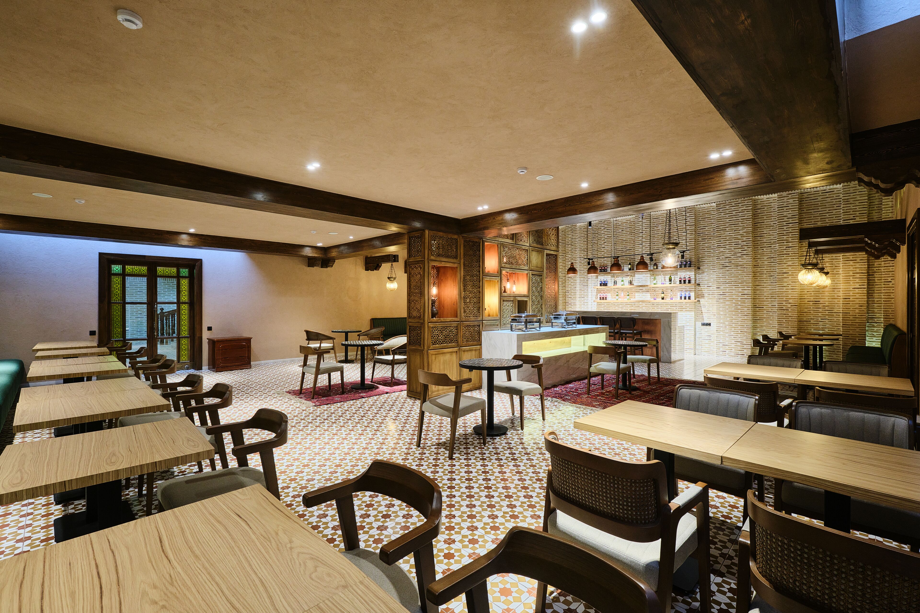 Un restaurant avec des tables et des chaises en bois, un coin bar et un sol à motifs.