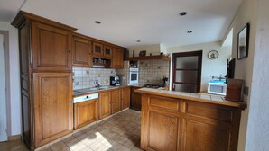 A kitchen with wooden cabinets, a tiled backsplash, a sink, a stove, and a microwave. - Proche Laguiole - Maison au Calme - vue Imprenable (Curières)