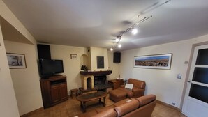 A living room with a fireplace, leather sofa, television, and tiled flooring. - Proche Laguiole - Maison au Calme - vue Imprenable (Curières)