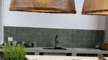 Una cocina con una isla central, dos taburetes de madera, un fregadero y dos grandes lámparas colgantes tejidas.