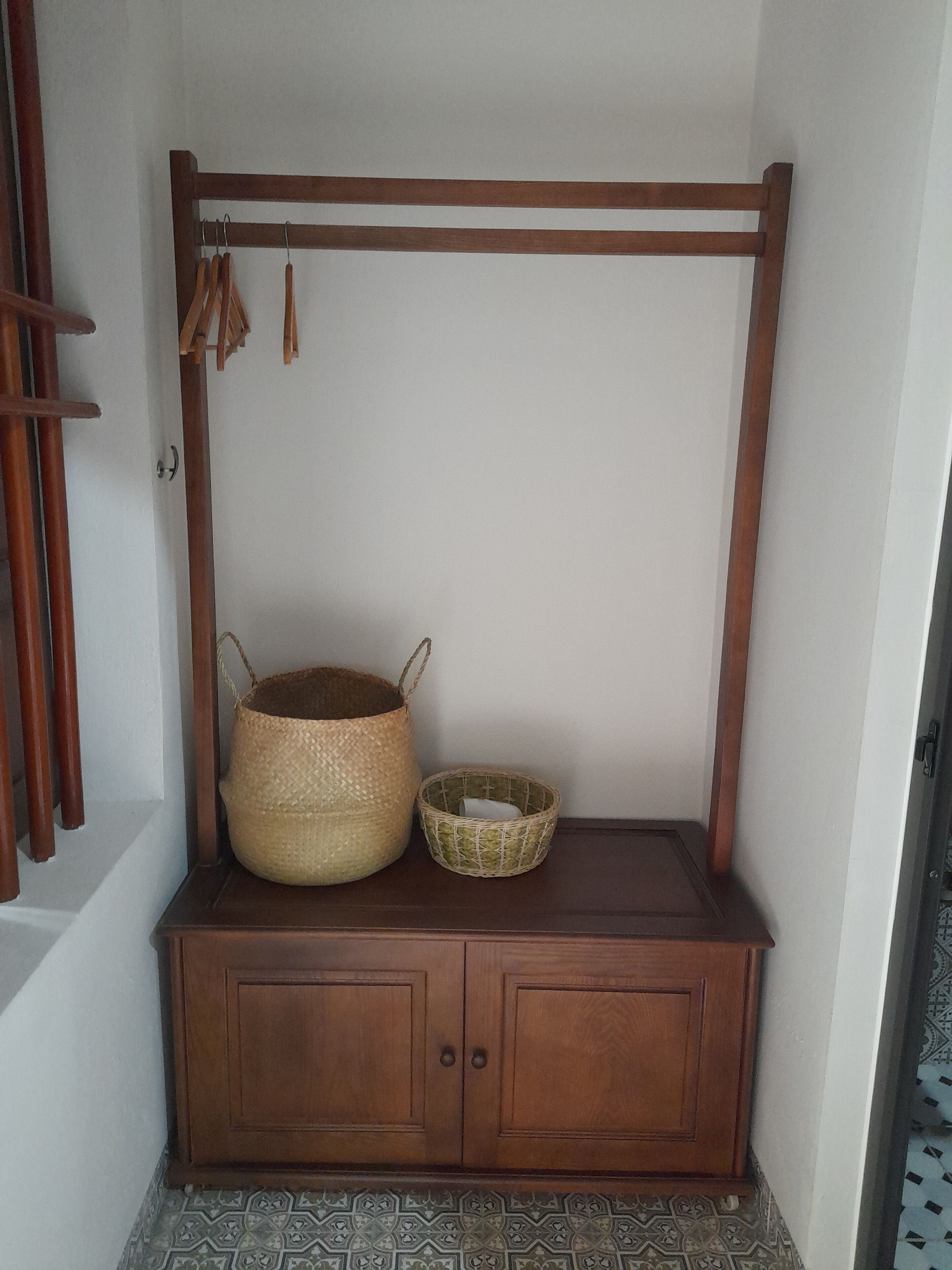 Un mueble de madera con dos cestas tejidas, una más grande y otra más pequeña, y un tendedero de madera con perchas de madera.