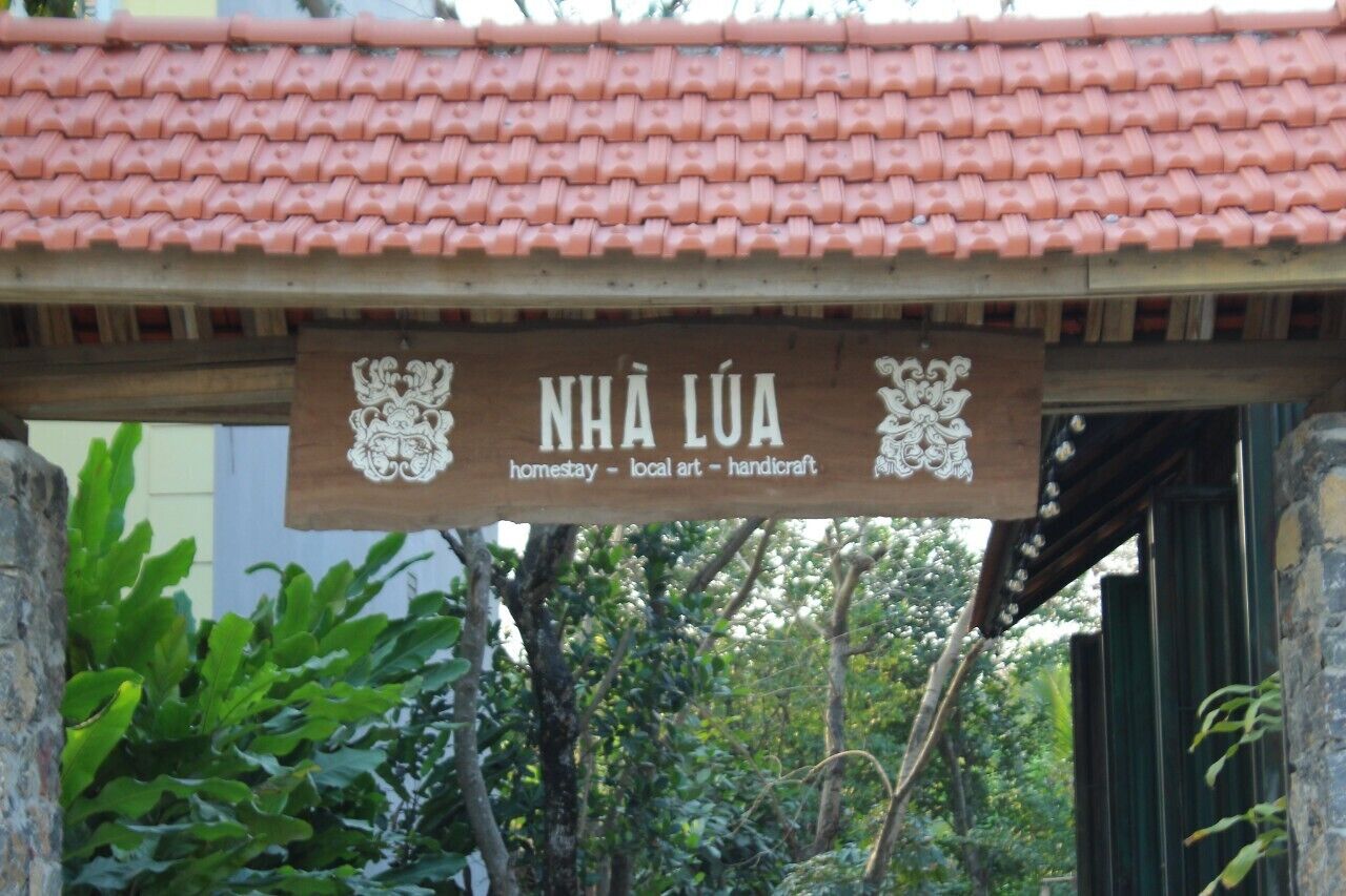 A wooden sign with the text "NHÃ LÃ" and "homestay - local art - handicraft" indicating a homestay experience.