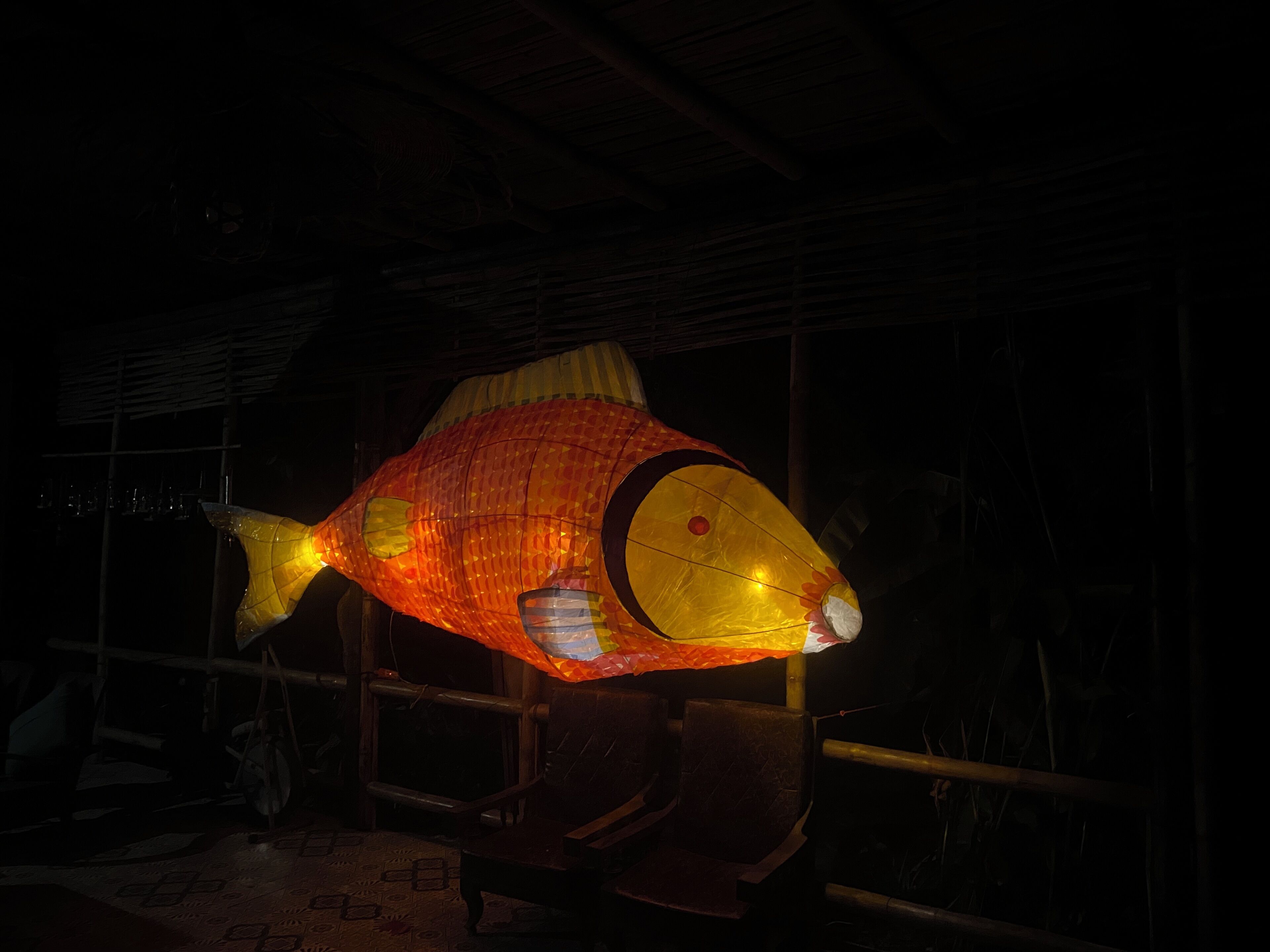Une lanterne en forme de poisson, suspendue dans une pièce faiblement éclairée et meublée de meubles en bois.