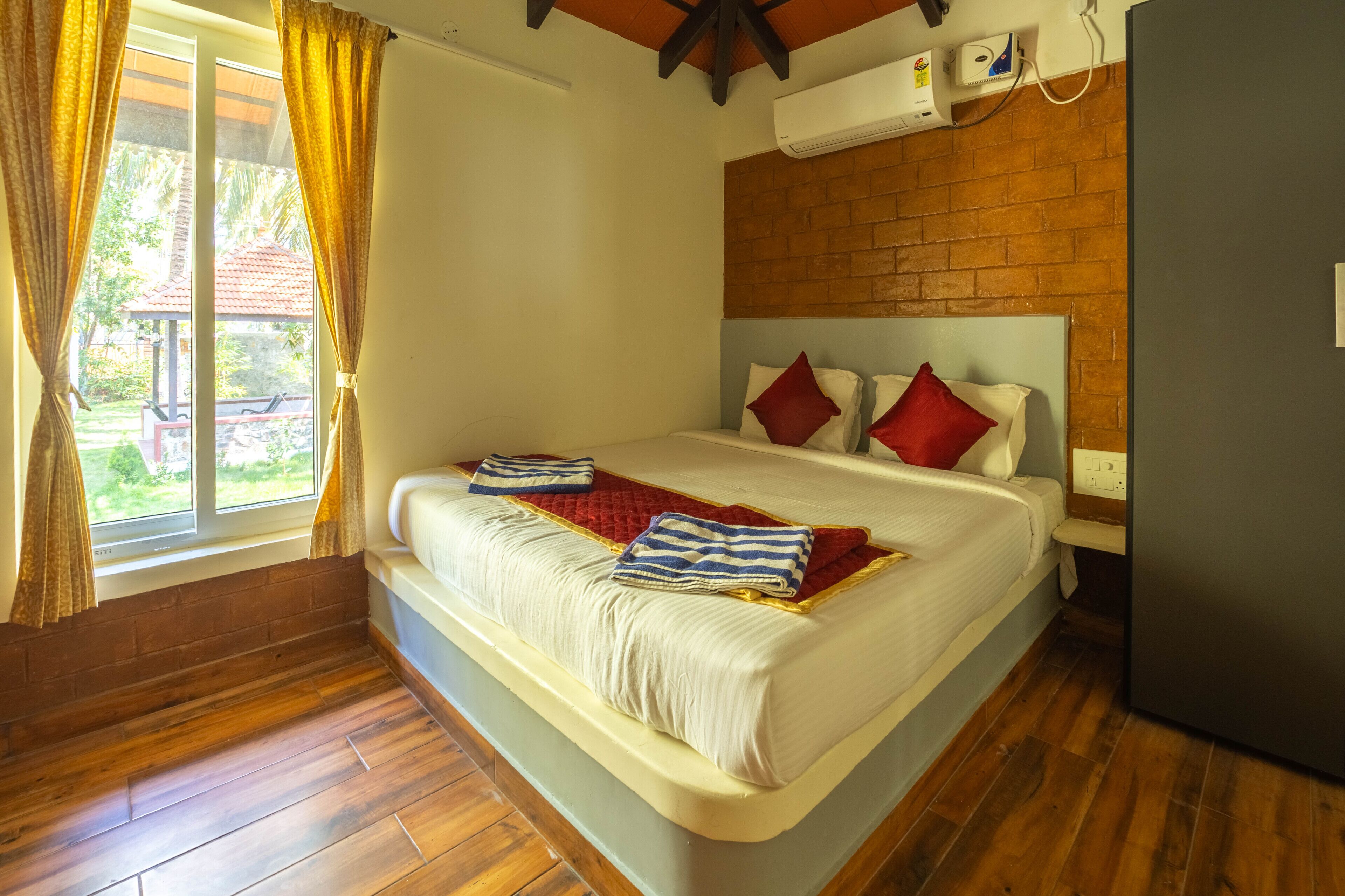 A bedroom with a large bed, wooden flooring, a brick wall, and a window with curtains.