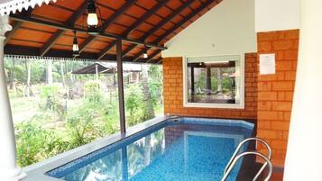 Una piscina con borde de azulejos, una escalera metálica y vistas a la vegetación.