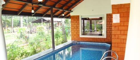 A swimming pool with a tiled edge, a metal ladder, and a view of greenery outside.