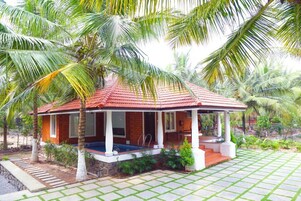 A bungalow with a tiled roof, a swimming pool, and a garden with palm trees.