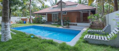 Una casa con piscina, rodeada de palmeras y un césped cuidado.