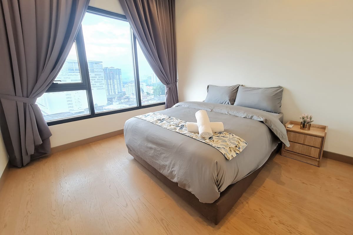Een moderne slaapkamer met een groot bed, grijs beddengoed en uitzicht op de stad door het raam.