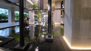 Un espacio interior moderno con piso reflectante, columnas estructurales y una escalera que sube a un nivel superior.