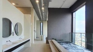 Un baño moderno con un banco alargado, un espejo grande y vistas de la ciudad a través de un ventanal.