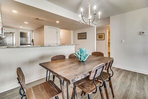 Un comedor con mesa y sillas de madera, una araña y una cocina al fondo.