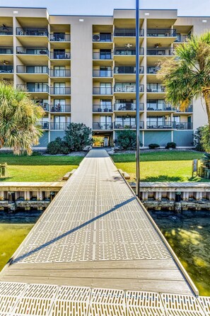 Un hotel de varios pisos con balcones, una pasarela de madera y una piscina.