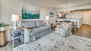Una sala de estar moderna con un sofá gris, un sillón estampado y un comedor con mesa y sillas.