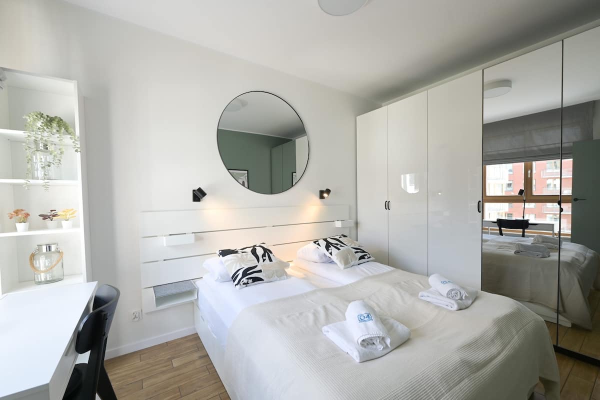 A modern hotel room with a bed, a desk, and a mirror.
