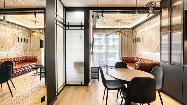 A modern interior with a wooden dining table, black chairs, a leather sofa, and a large window with a view.