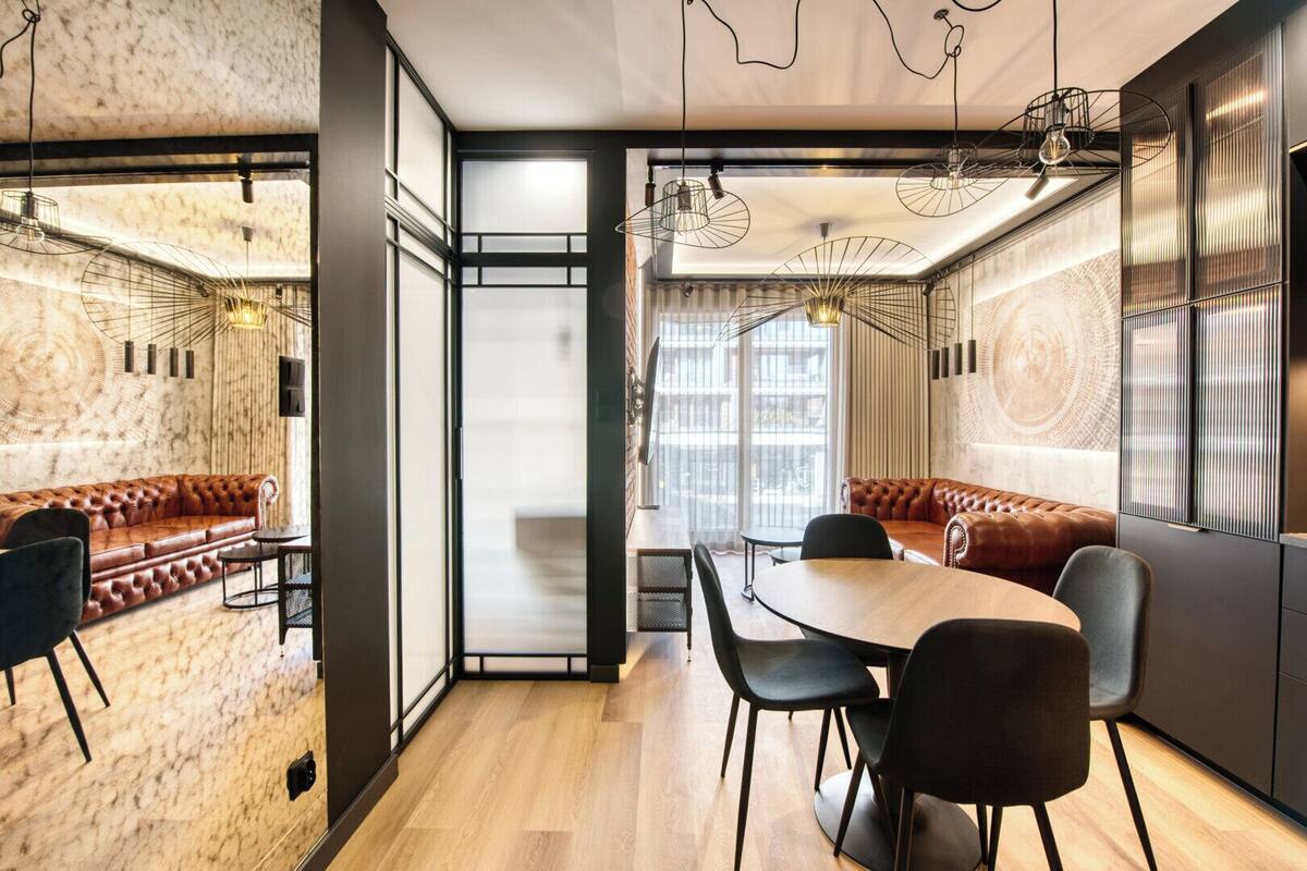 A modern interior with a wooden dining table, black chairs, a leather sofa, and a large window with a view.