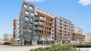 A multi-story residential building with balconies, a parking area, and a clear sky.
