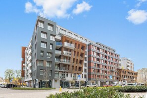A multi-story residential building with balconies, a parking area, and a clear sky.