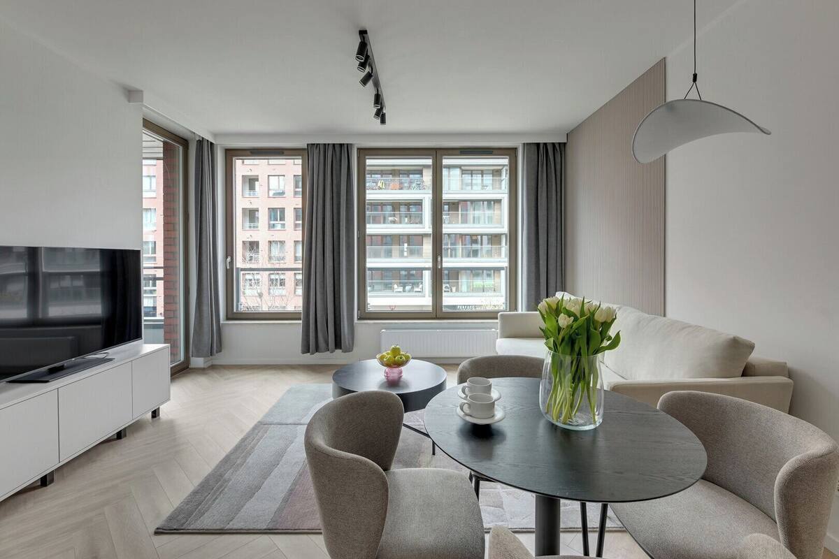A modern living room with a flat-screen TV, a round dining table, and a sofa.