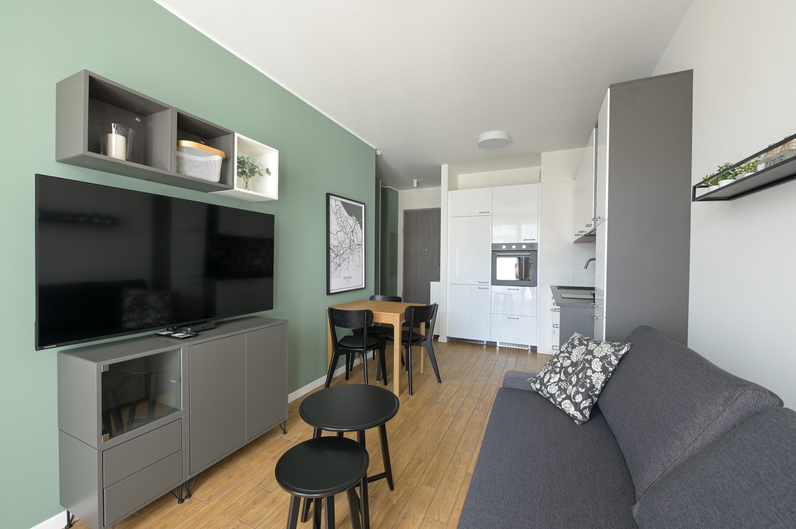 Un espacio habitable compacto con comedor, kitchenette y un televisor de pantalla plana montado en un mueble.