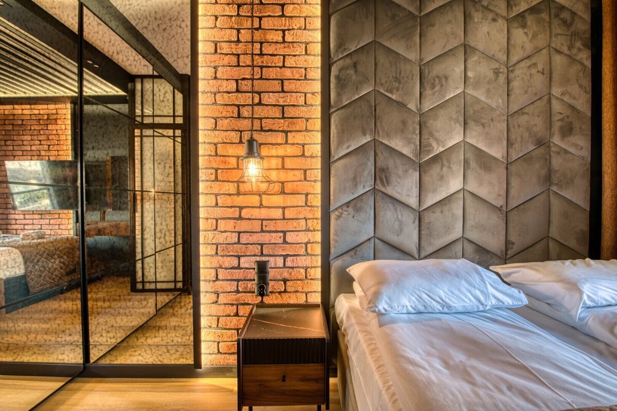 Une chambre moderne avec un mur en briques, une tête de lit à motifs géométriques et une cloison en verre.