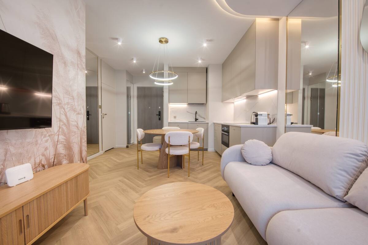 A modern living room with a sofa, a round wooden coffee table, and a TV on a wooden cabinet.