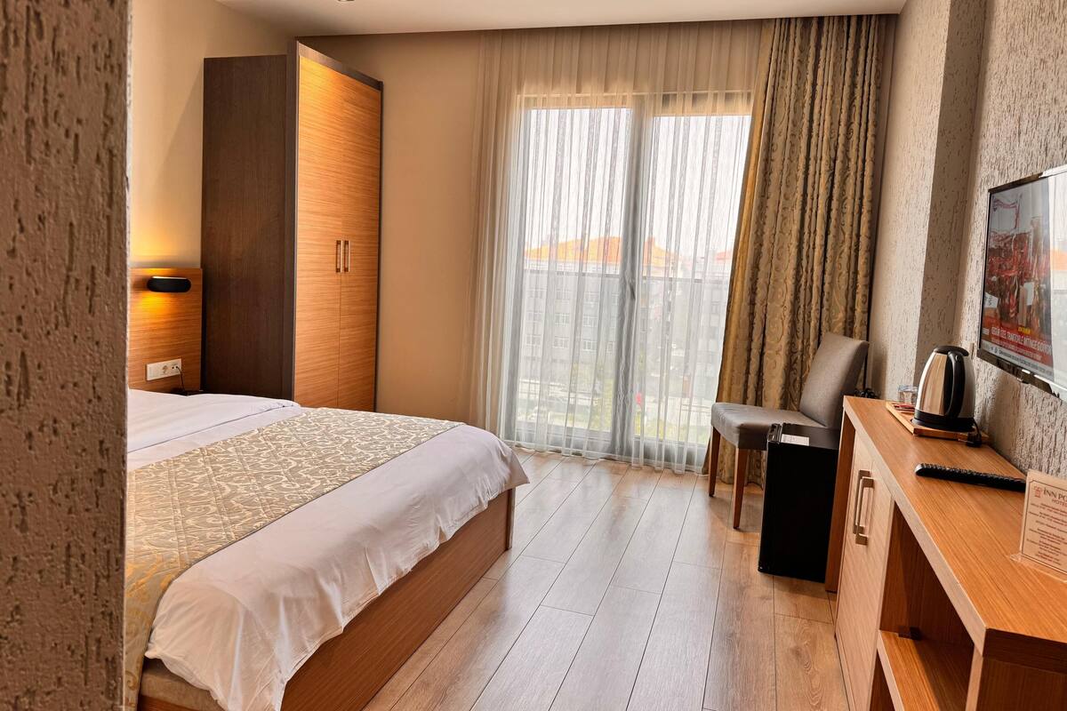A hotel room with a bed, a desk, a chair, and a large window with curtains.