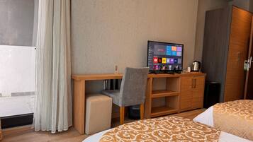 Quarto de hotel com cama, escrivaninha com cadeira, televisão e guarda-roupa.