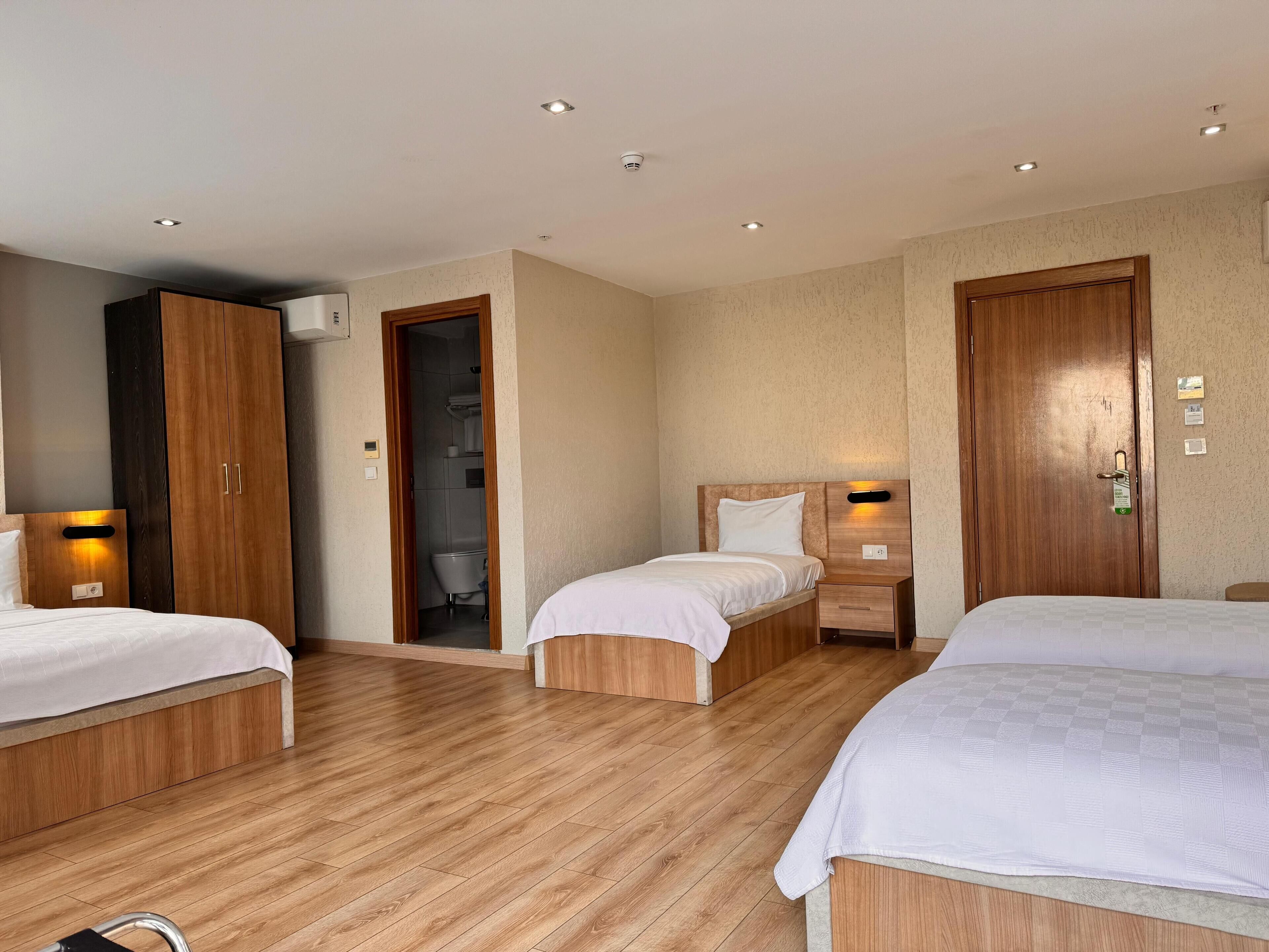 A hotel room with two beds, wooden flooring, a wardrobe, a bathroom with a shower, and a door with a lock and keycard slot.