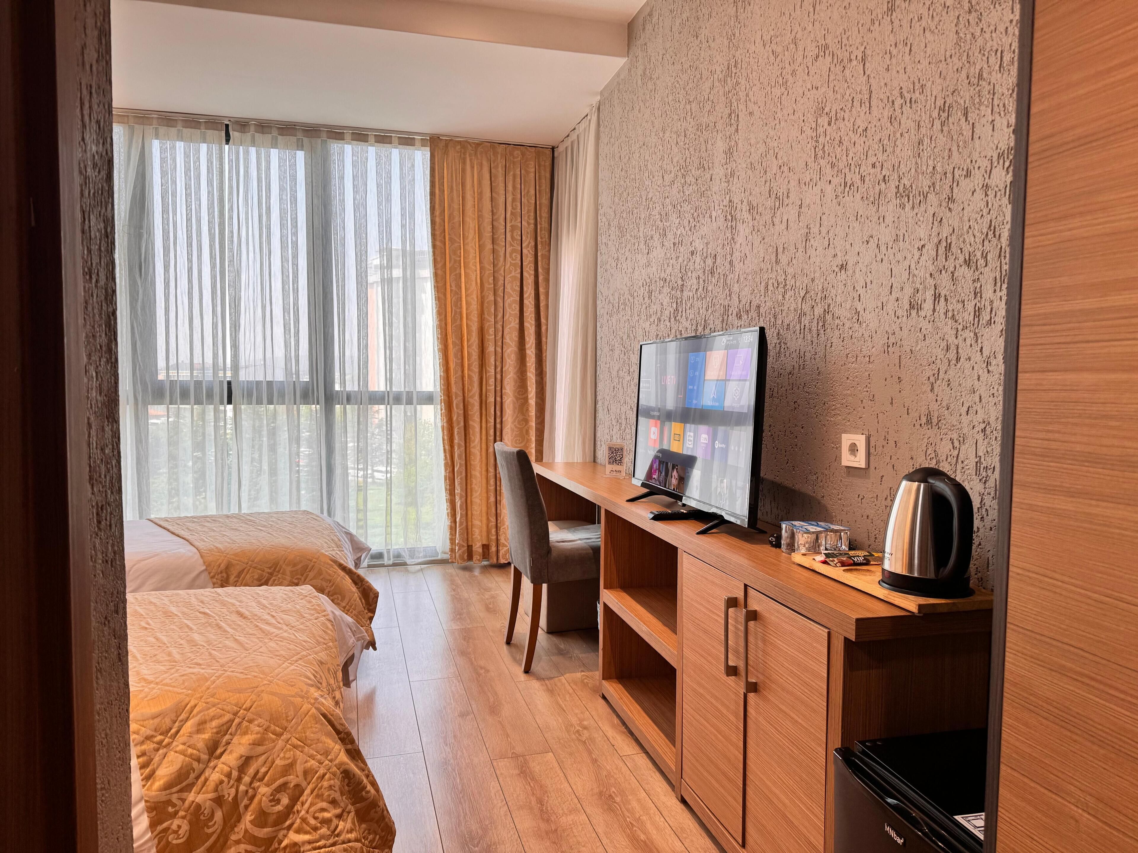 Habitación de hotel con cama, escritorio con computadora, cafetera y vista al exterior.