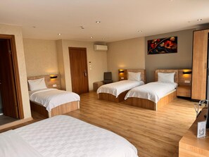 Quarto de hotel com duas camas de solteiro, um guarda-roupa de madeira, uma escrivaninha com cadeira e um quadro na parede.