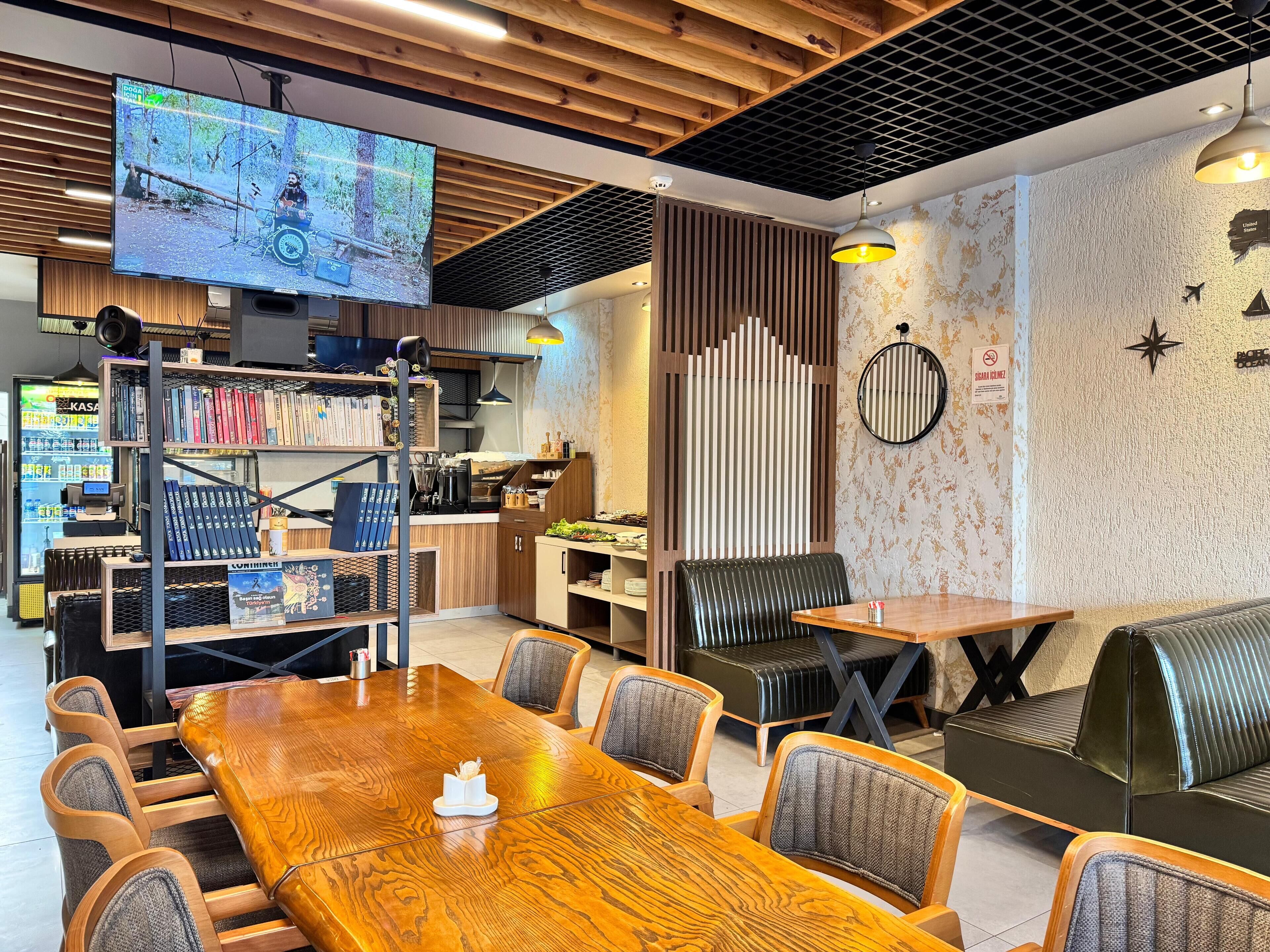 Un restaurante moderno con techo de madera, una gran pantalla de televisión, estanterías y un área de estar con mesas y sillas.