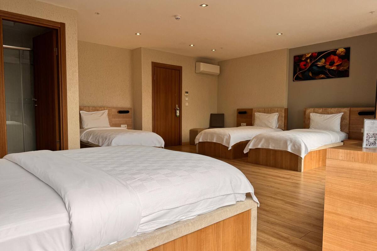 A hotel room with two single beds, a wooden floor, a painting on the wall, and an air conditioning unit.