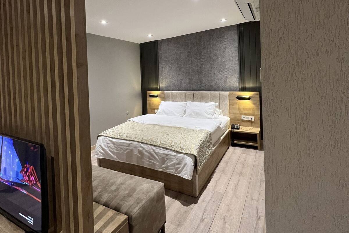 A modern bedroom with a bed, bedside tables, a TV, and a wooden partition.