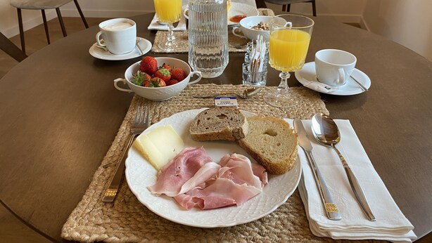 A breakfast setting with a plate of ham, cheese, and bread, a bowl of strawberries, and glasses of orange juice on a woven placemat. - CasaOssan (San Pietro in Cariano)